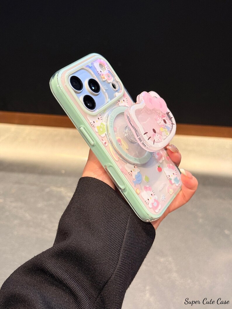 May include: A mint green phone case with a clear back featuring a repeating pattern of cartoon characters. The case has a matching pop-up grip with a pink bow and a cartoon face. The text "Super Cute Case" is visible.