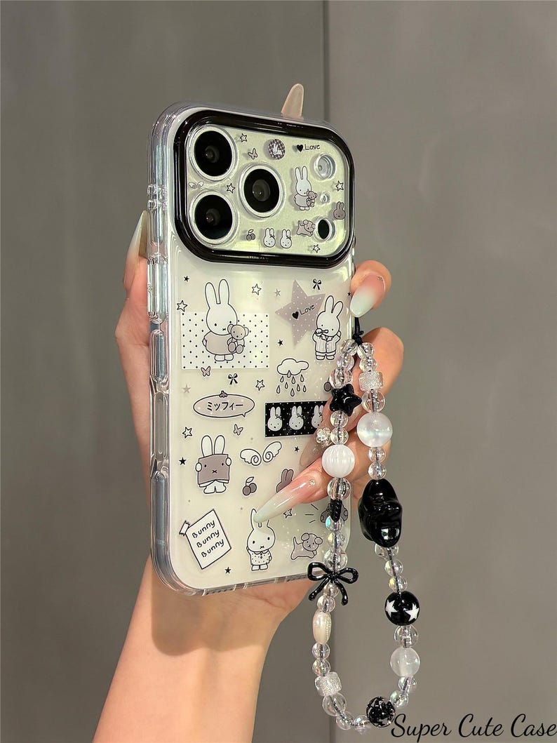Pode incluir: Capa de telefone transparente com um design de coelho branco e preto. A capa tem uma al&ccedil;a de contas com contas pretas e brancas, um la&ccedil;o preto e um pingente de caveira preta. A capa tem as palavras "Bunny Bunny Bunny" e "Super Cute Case".