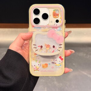 Peut inclure: Une coque de t&eacute;l&eacute;phone jaune avec des personnages Hello Kitty et un n&oelig;ud rose. La coque a un dos transparent et un bord jaune. Le design comprend diverses illustrations Hello Kitty et le texte "Hello Kitty".