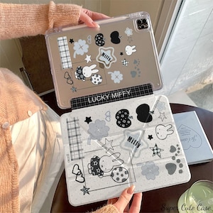 Könnte beinhalten: Transparente Tablet-Hülle mit weißem und grauem Miffy-Design. Die Hülle hat einen schwarzen Rand mit dem Text "LUCKY MIFFY". Das Design umfasst Sterne, Kleeblätter und eine Hasenillustration.