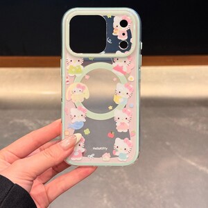 May include: A clear phone case featuring a pink and mint green border with Hello Kitty characters. The case has a clear center and a camera cutout. The Hello Kitty characters are in various poses and outfits. The text "HelloKitty" is printed on the case.