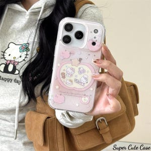 May include: Clear iPhone case with a pink apple design featuring Hello Kitty characters. The case has a clear border and a pink background with small stars and apple illustrations. The text "Super Cute Case" is at the bottom.