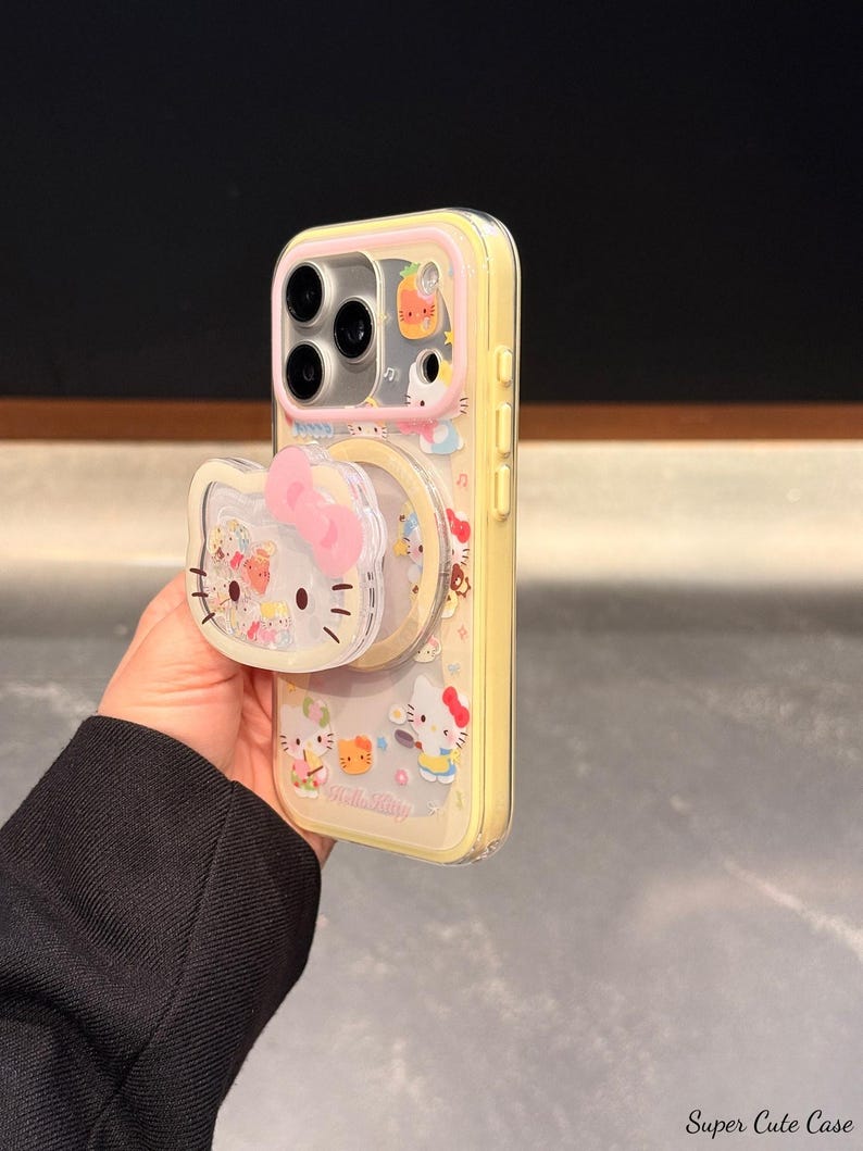 Peut inclure: Coque de t&eacute;l&eacute;phone jaune avec des personnages Hello Kitty et une poign&eacute;e pop-up. L'&eacute;tui a un dos transparent avec un bord jaune et un n&oelig;ud rose sur la poign&eacute;e pop-up. L'&eacute;tui est d&eacute;cor&eacute; de diverses illustrations Hello Kitty.