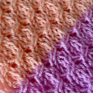May include: Close-up of a knitted fabric with a gradient of peach and purple. The fabric has a sparkly texture.