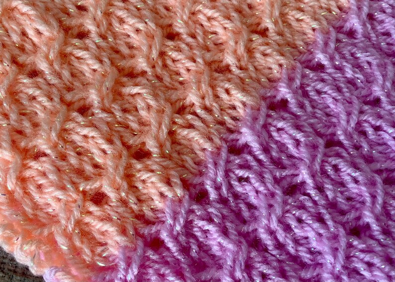 May include: Close-up of a knitted fabric with a gradient of peach and purple. The fabric has a sparkly texture.