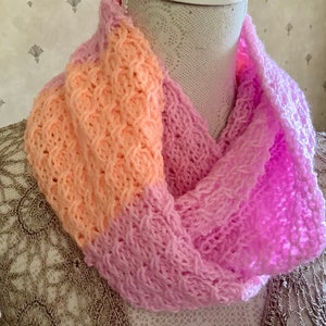 May include: A knitted scarf with a pink and peach color gradient. The scarf is made with a delicate, openwork stitch.