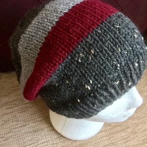 May include: A gray, red, and white striped knit beanie hat with a slouchy fit.