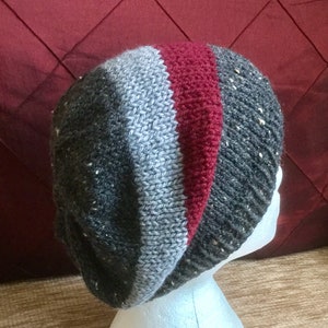 May include: A gray, red, and white striped knit beanie hat with a slouchy fit.