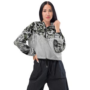Puede incluir: Una chaqueta cortavientos corta con cuello de media cremallera y dobladillo con cordón. La parte superior presenta un estampado de leopardo en gris, negro y blanco, mientras que la inferior es de color gris claro liso. Flores negras en las mangas.