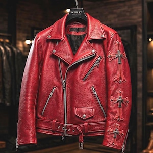 May include: A red leather jacket with a classic biker style. Features include a notched collar, asymmetrical zipper, multiple pockets, and a belt at the waist. The sleeves are adorned with cross-shaped embellishments. The jacket is hanging on a black hanger.