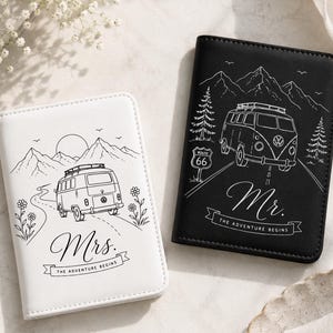 May include: A white passport holder with a black line drawing of a van, mountains, and the text Mrs. The Adventure Begins, and a black passport holder with a white line drawing of a van, mountains, a Route 66 sign, and the text Mr. The Adventure Begins.
