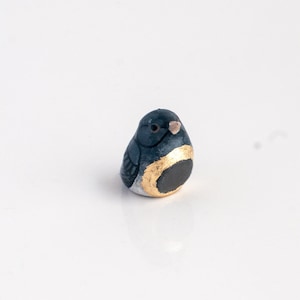 Peut inclure: Une petite figurine d'oiseau en céramique peinte à la main. L'oiseau est bleu avec un ventre blanc et une bande dorée autour du corps.