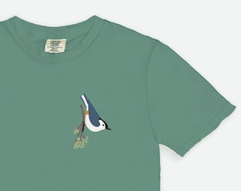 May include: A green t-shirt with a white-breasted nuthatch perched on a branch with pink flowers.