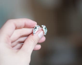 Puede incluir: Un par de pendientes de plata con un diseño detallado de un pájaro con marcas negras y blancas.