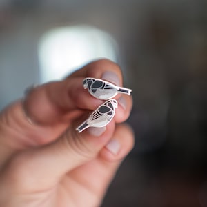 May include: A pair of silver earrings featuring a black and white bird design.