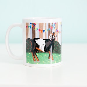 May include: White ceramic mug with a colorful illustration of a spotted goat standing in a field with trees and bunting in the background.