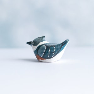 May include: Hand-painted ceramic bird figurine with blue, white, and brown accents. The bird is in a sitting position with its head turned to the side.