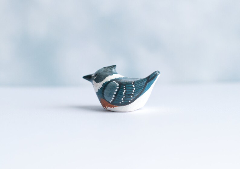 May include: Hand-painted ceramic bird figurine with blue, white, and brown accents. The bird is in a sitting position with its head turned to the side.
