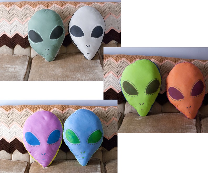 May include: Six alien-shaped pillows in various colors, including green, white, orange, blue, and purple. The pillows are all on a brown and white patterned couch.