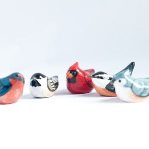 Peut inclure: Une collection de cinq petites figurines d'oiseaux color&eacute;s. Les oiseaux sont peints dans diverses couleurs, dont le rouge, le bleu, le noir, le blanc et l'orange. Chaque oiseau a un design et une pose uniques.