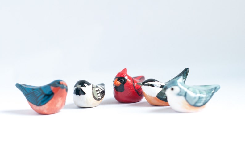 Peut inclure: Une collection de cinq petites figurines d'oiseaux color&eacute;s. Les oiseaux sont peints dans diverses couleurs, dont le rouge, le bleu, le noir, le blanc et l'orange. Chaque oiseau a un design et une pose uniques.