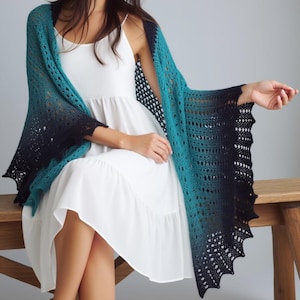 May include: A teal and navy blue shawl with a gradient effect. The open-weave shawl is draped over the shoulders. The shawl has a scalloped edge and is made of a soft, lightweight material.