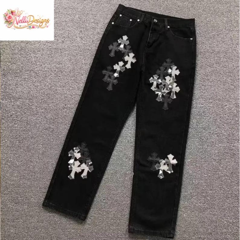 May include: Black denim jeans with decorative cross appliques in shades of gray and white. The jeans have a classic five-pocket design and a straight leg fit. The crosses are clustered on the front and back of the jeans.