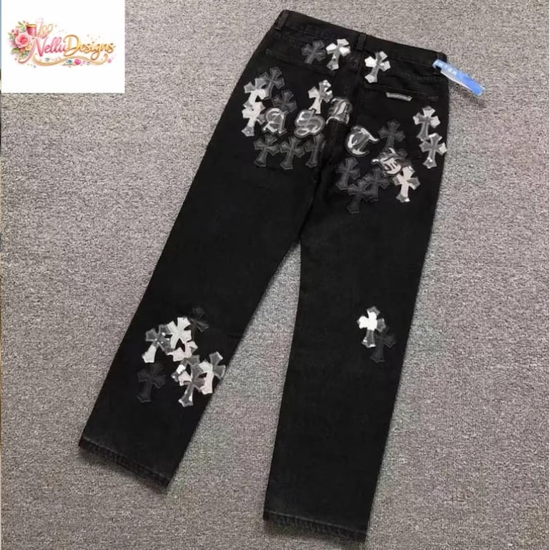 May include: Black denim jeans with multiple cross-shaped embellishments in silver and white. The jeans have a classic five-pocket design and a straight leg fit. The embellishments are clustered on the front and back of the jeans.