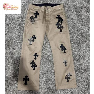 Pu&ograve; includere: Pantaloni color cachi con multiple toppe a forma di croce nera, alcune con motivo a scacchi. I pantaloni hanno un classico design a cinque tasche e una cintura blu scuro. L'immagine mostra anche un logo nell'angolo in alto a sinistra.