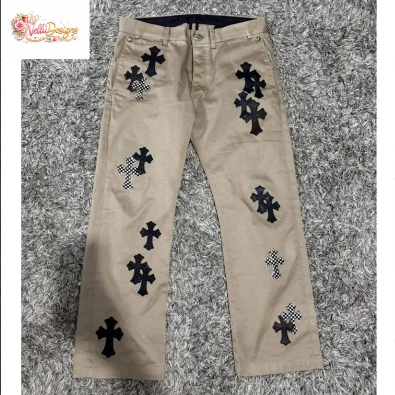 Pu&ograve; includere: Pantaloni color cachi con multiple toppe a forma di croce nera, alcune con motivo a scacchi. I pantaloni hanno un classico design a cinque tasche e una cintura blu scuro. L'immagine mostra anche un logo nell'angolo in alto a sinistra.