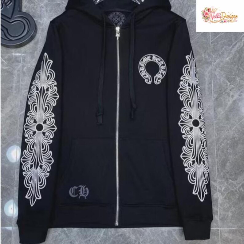 May include: Black zip-up hoodie with white ornate cross designs on the sleeves and a circular emblem on the chest. Features a silver zipper and the letters "CH" embroidered on the lower left. The hoodie has a hood and a small logo in the upper right corner.