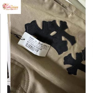 Pu&ograve; includere: Pantaloni chino color cachi con applicazioni a forma di croce in pelle nera. Un'etichetta del prodotto &egrave; attaccata. I pantaloni hanno uno stile classico, adatti all'uso quotidiano.