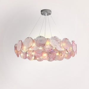 Könnte beinhalten: Ein moderner Kronleuchter mit einem kreisförmigen Design aus zahlreichen rosa, scheibenförmigen Glaselementen. Die Leuchte hängt an einer silberfarbenen Deckenhalterung und erzeugt ein weiches, umgebendes Leuchten.