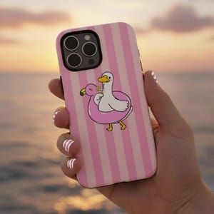 May include: Pink and white striped phone case featuring a cartoon duck and flamingo in a pool float. The duck is holding a drink. The case has a black border and a camera cutout.