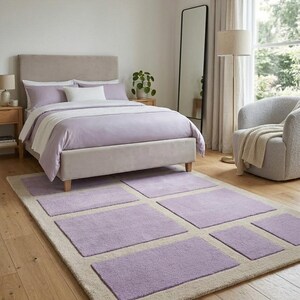 May include: A bedroom scene featuring a bed with lavender bedding and a matching area rug. The rug has a beige border with lavender rectangular inserts. A tall mirror and a cozy armchair complete the room's decor.