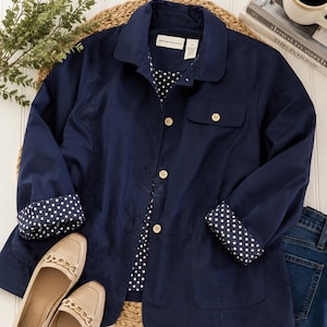 Peut inclure: Une veste bleu marine avec un col, des manches longues à revers à pois blancs et une doublure assortie à pois blancs. La veste présente une fermeture boutonnée sur le devant avec des boutons clairs, une poche poitrine et deux poches inférieures. L'étiquette indique Alfred Dunner.