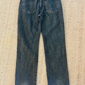 K&ouml;nnte beinhalten: R&uuml;ckansicht einer blauen Jeans mit zwei Ges&auml;&szlig;taschen und einem Wrangler-Etikett. Die Jeans hat ein klassisches F&uuml;nf-Taschen-Design und eine gerade Beinpassform. Der Denim hat einen verblichenen, abgenutzten Look.