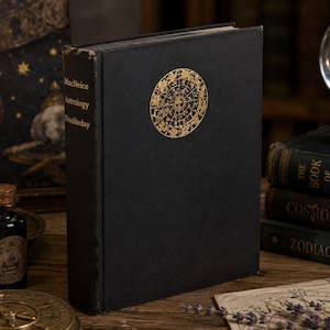 May include: A black book titled "MacNeice Astrology Doubleday" with a gold celestial design on the cover. The book is standing upright on a wooden surface, with other books and a candle in the background. The book's cover has a circular gold design.