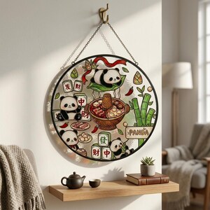 Puede incluir: Arte de ventana de vidriera redonda con pandas disfrutando de una comida de olla caliente. El diseño incluye bambú, chiles y caracteres chinos. La ventana está enmarcada en negro y cuelga de una cadena.