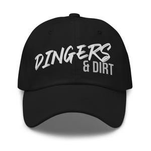 May include: Black baseball cap with the text "DINGERS & DIRT" in white, stylized lettering. The cap has a curved brim and a button on top. A casual accessory for outdoor activities.