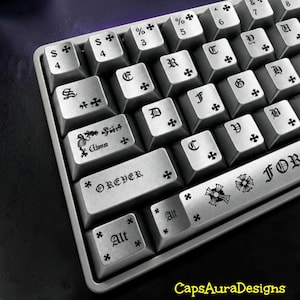May include: A silver mechanical keyboard with custom keycaps featuring black gothic-style lettering, cross symbols, and decorative flourishes. The spacebar displays the text FOREVER, while other keys show letters, numbers, and the word Alt.