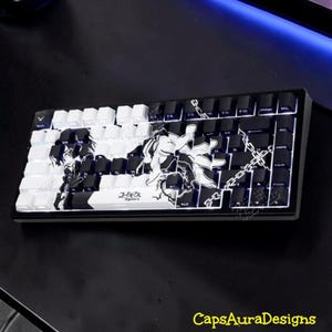 May include: A mechanical keyboard featuring a black and white custom keycap set with an anime-style illustration of a character and chains. The spacebar displays the Japanese text Code Geass. The keys are arranged in a standard layout with white and black keys.