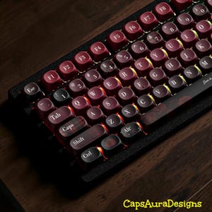 May include: A mechanical keyboard featuring deep maroon, circular keycaps with white lettering. The keyboard includes a black frame, orange backlighting, and a spacebar decorated with a rose pattern. The text CapsAuraDesigns appears at the bottom.