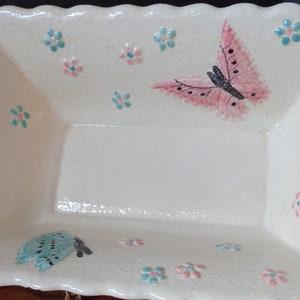 May include: A white ceramic serving dish with a scalloped edge. The dish is decorated with pink and blue butterflies and flowers.