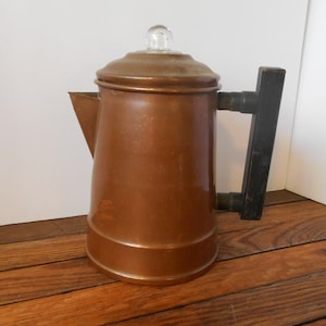 May include: A vintage copper percolator coffee pot with a glass lid and a wooden handle.