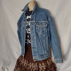 May include: A blue denim jacket with a brown skirt with floral embroidery. The jacket has a button closure and two pockets on the front.