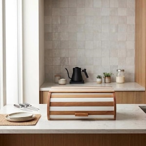 Pode incluir: Uma caixa de pão de madeira com tampa enrolável. A caixa apresenta listras alternadas de madeira clara e branca. Uma pequena alça de madeira está na frente. A caixa de pão está em uma bancada com um backsplash de azulejos de cor neutra.