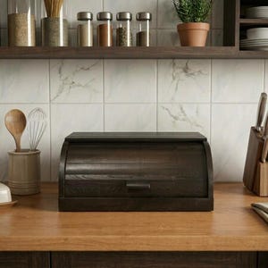 May include: A dark brown wooden bread box with a roll-top lid and a small handle, positioned on a wooden countertop. The bread box features a horizontal slatted design and a smooth finish, providing a storage solution for kitchen items.