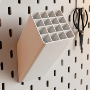 Peut inclure: Un organisateur en plastique blanc avec un dessus inclin&eacute; et seize compartiments carr&eacute;s, con&ccedil;u pour &ecirc;tre fix&eacute; sur un panneau perfor&eacute;. L'organisateur pr&eacute;sente un corps solide et inclin&eacute; qui s'&eacute;tend vers l'ext&eacute;rieur du mur pour le rangement.