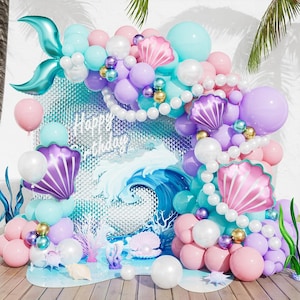 May include: A mermaid-themed balloon arch featuring a teal foil mermaid tail, purple and pink shell-shaped balloons, and a backdrop with a wave graphic and the text Happy Birthday. The arrangement includes white, teal, and purple balloons.